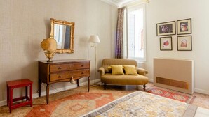 A hotel room with a vintage sofa, a wooden dresser, a small red table, a large bed with a patterned bedspread, a floor lamp, and a radiator. - Charming apartment not far from Piazza San Marco (Venezia)