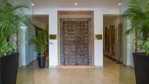 Un couloir avec une porte décorée de motifs, des plantes en pot et un sol carrelé.