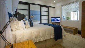 Une chambre à coucher comprenant un lit, un bureau, une chaise, un téléviseur et une fenêtre avec des stores.