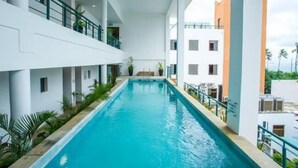 Une piscine offrant une vue sur un immeuble doté de balcons et d’une façade blanche.