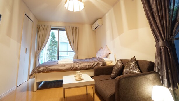 Een slaapkamer met een bed, een bank, een klein tafeltje en een raam met gordijnen.
