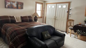 Une chambre à coucher comprenant un lit, un fauteuil en cuir noir, une chaise en bois, une table avec une lampe et une porte avec des fenêtres.