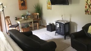 Un salon avec un canapé, un téléviseur fixé au mur, une petite table et une plante.