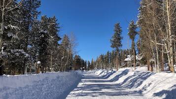 A snow-covered road flanked by tall evergreen trees under a clear blue sky.