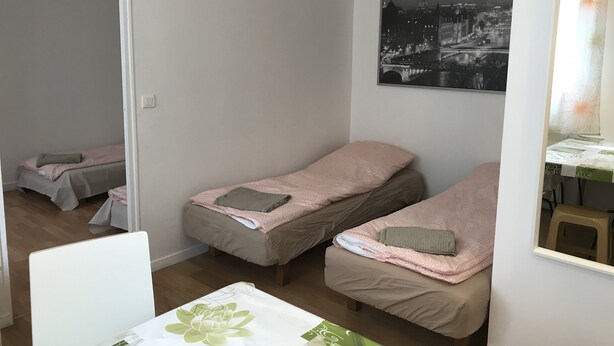 Pieni, siisti huone, jossa on kaksi erillistä sänkyä, kukkapainokuosinen pöytäliina ja kaupunkimaisemaa esittävä valokuva seinällä.