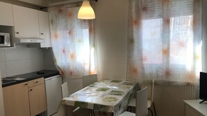 Kompakti keittiö, jossa on ruokapöytä, tuolit, mikroaaltouuni ja riippuvalaisin.