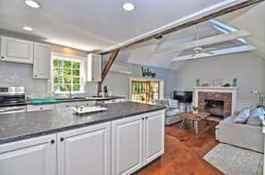 Een ruime keuken met witte kastjes, een granieten aanrechtblad en een groot eiland. In de woonkamer is een open haard met een televisie en comfortabele zitplaatsen.