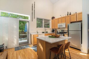 Una cocina moderna con armarios de madera, una isla central, taburetes de bar, un refrigerador y un microondas.