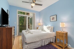 Un dormitorio con cama, mesitas de noche, ventilador de techo y puerta corrediza de vidrio que da a un espacio exterior.