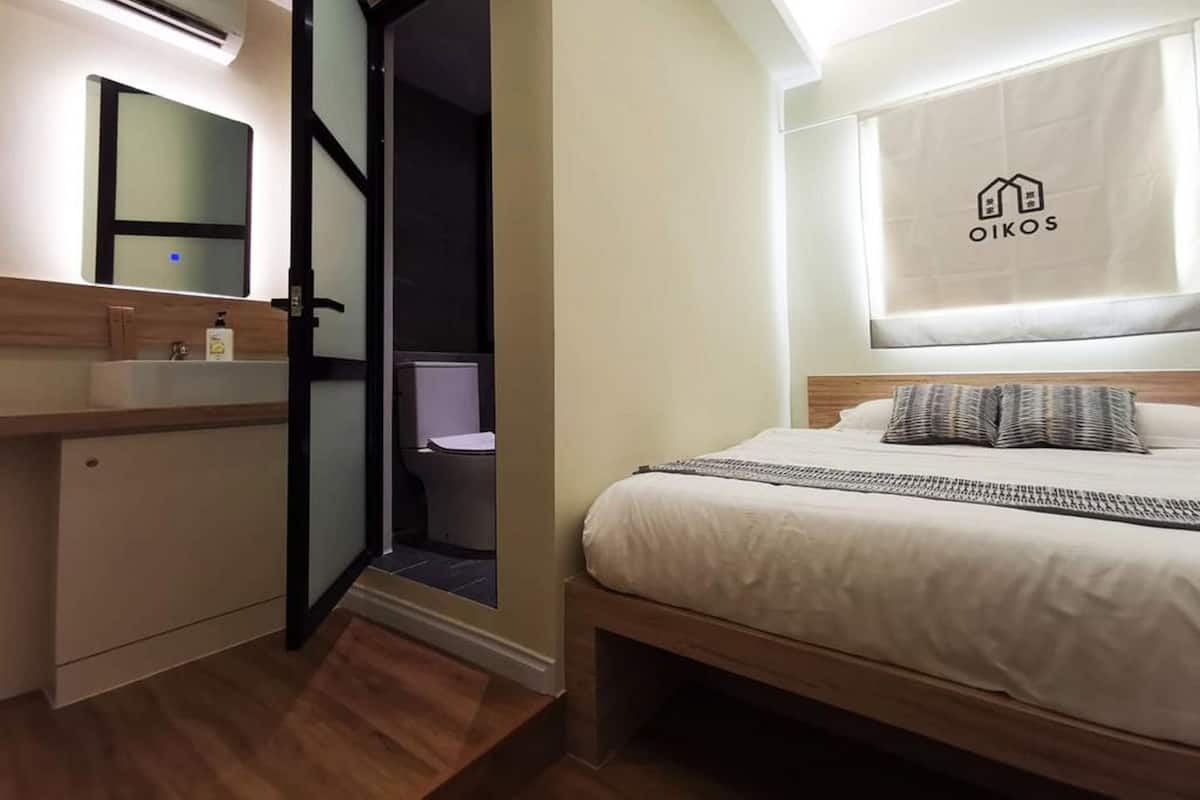 A modern hotel room with a bed, a bedside table, a mirror, and a bathroom visible through an open door.