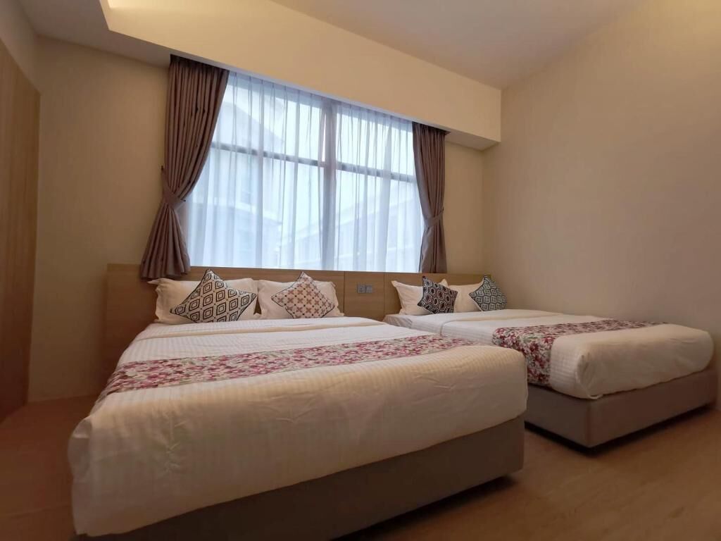 A hotel room with two beds, a large window with curtains, and a neutral color scheme.