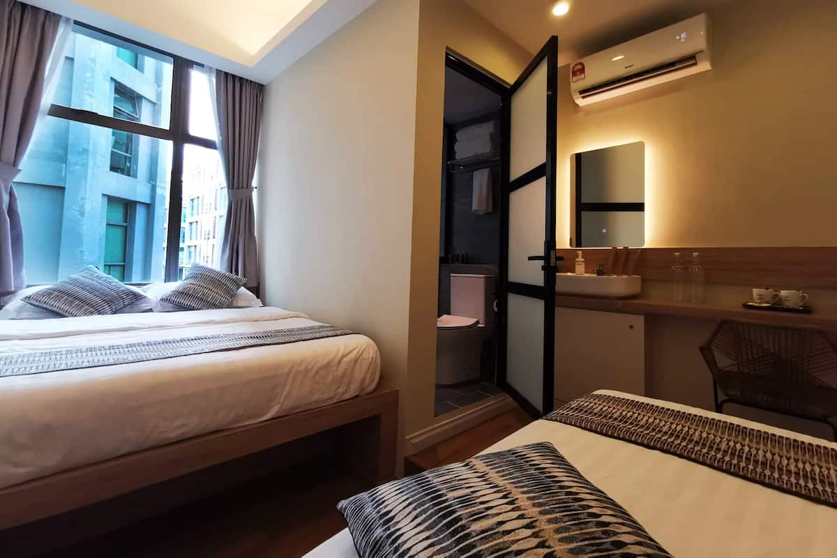A hotel room with two beds, a bathroom with a sink and mirror, and an air conditioning unit.