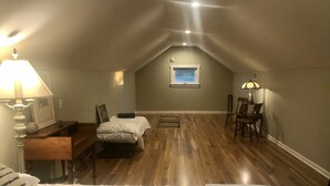 A cozy attic bedroom with a wooden floor, a bed, a desk, and a chair. There is a window with a view of the sky. - 4 bedroom, 116 acre Farmhouse 10 minutes from downtown  Charlevoix  (Charlevoix)
