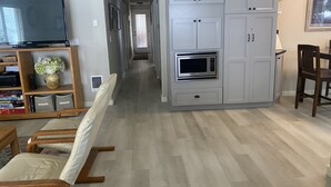 A modern living room with a flat-screen TV, a wooden entertainment unit, a dining area with a table and chairs, and a kitchen with built-in appliances. - 3 bedrooms, 2 bathrooms (Sisters)