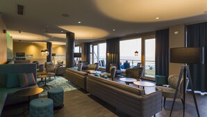 Een moderne hotellobby met een zithoek, een bar en grote ramen met uitzicht op de zee.