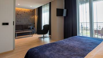 Una camera d'albergo moderna con un letto, una poltrona, una televisione e ampie finestre.