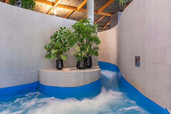 Un jacuzzi con borde azul, rodeado de paredes de azulejos y vigas de madera.