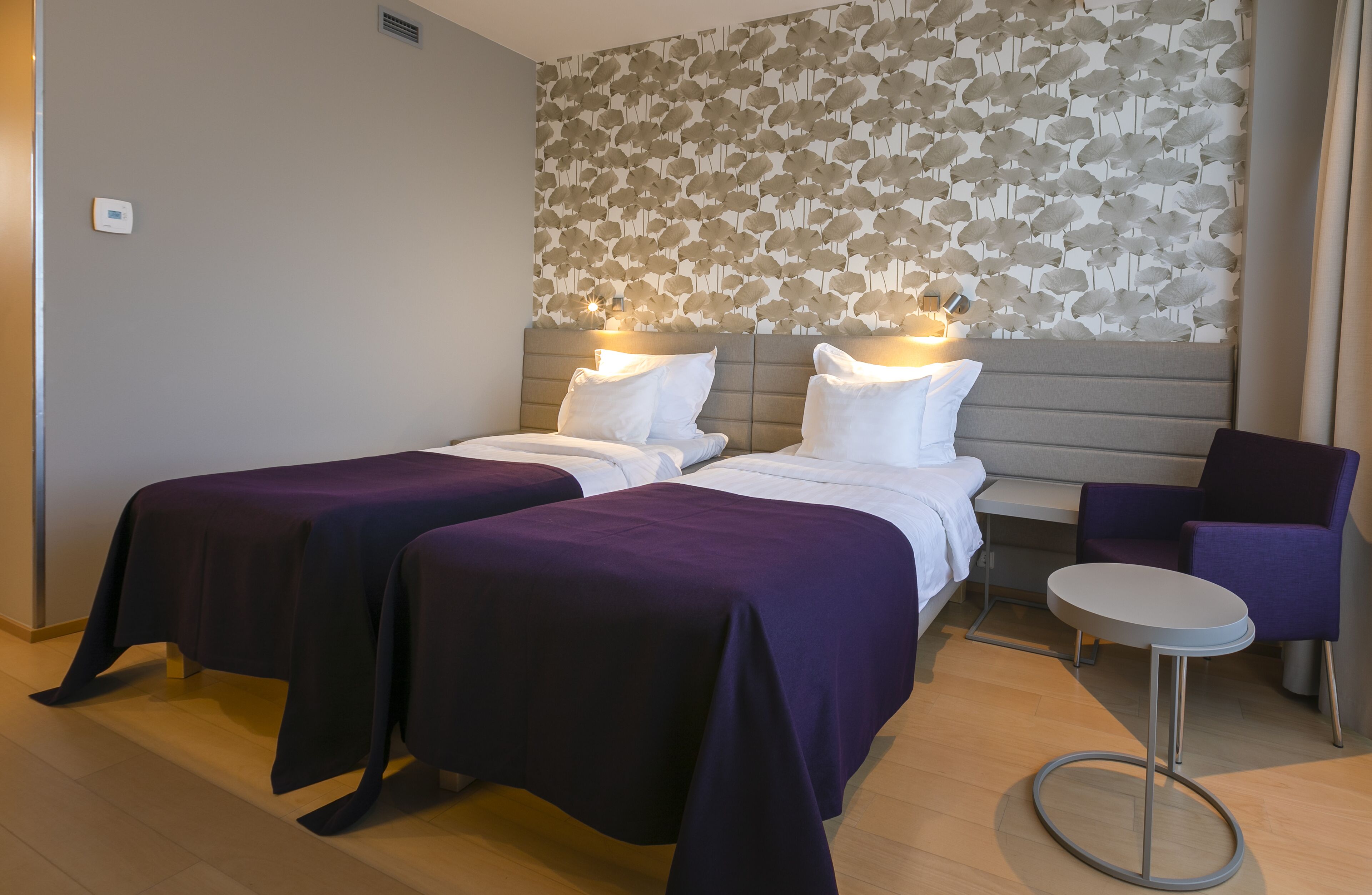 A hotel room with two beds, a small round table, and a purple chair.