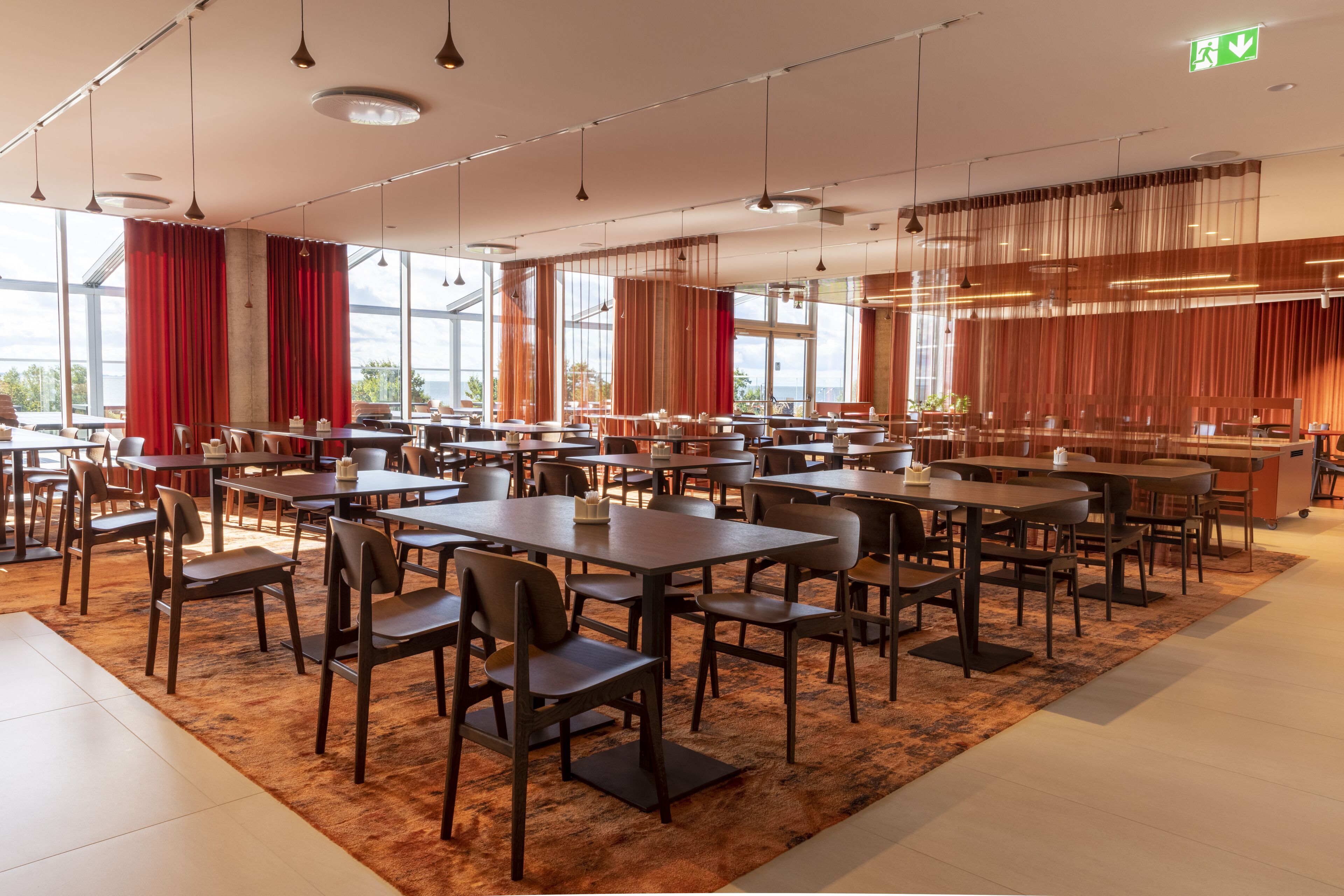 Ein geräumiger Essbereich mit mehreren Tischen und Stühlen, großen Fenstern und einem modernen Interieur.