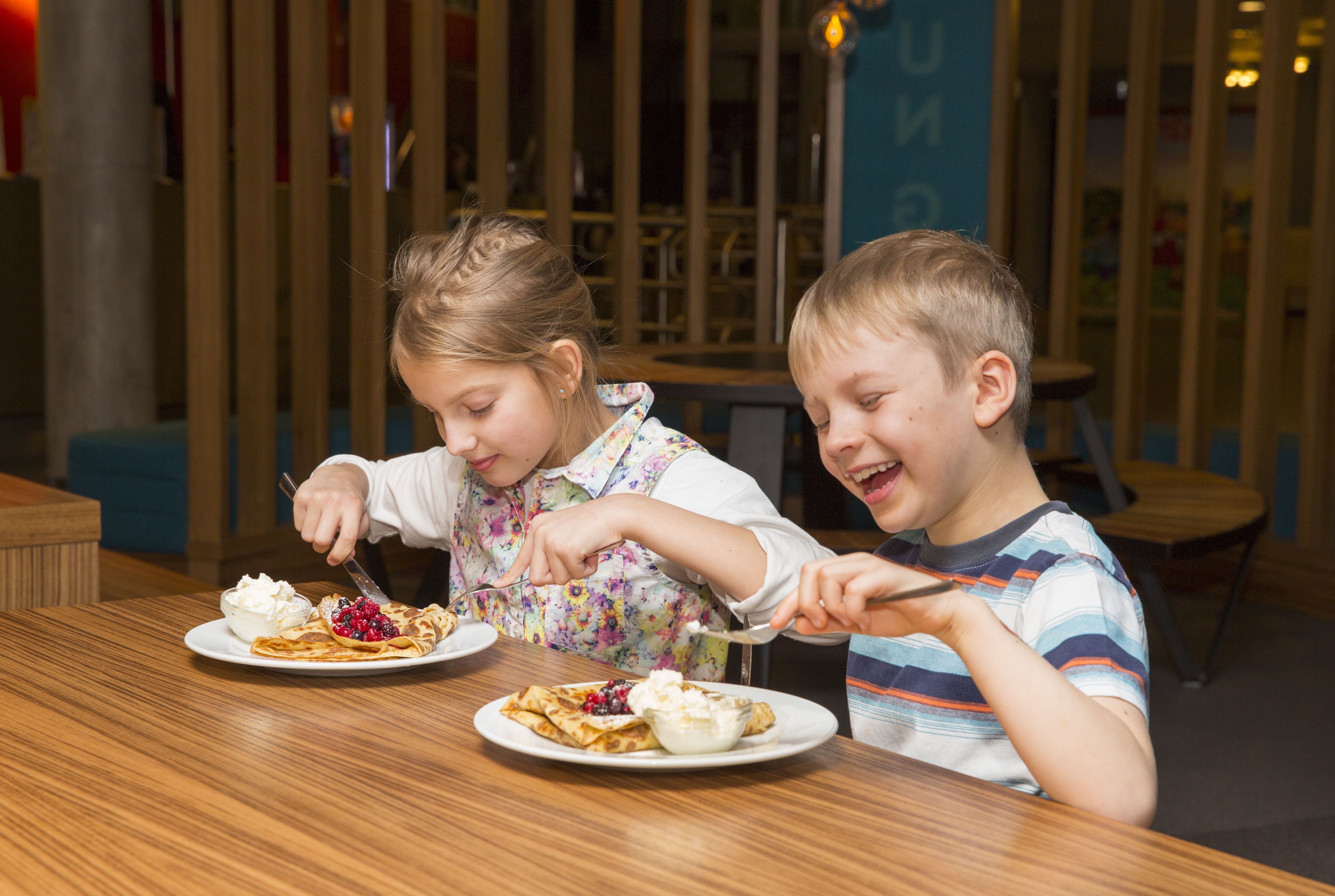 Deux enfants sont assis à une table en bois dans un restaurant dont l’intérieur présente un design moderne.
