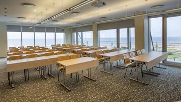 Une salle de conférence équipée de tables et de chaises, de grandes fenêtres donnant sur la mer et d’un sol recouvert de moquette.
