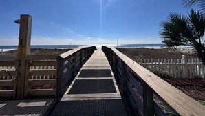 A wooden boardwalk leading to a beach with a palm tree on the right. - Time to get… 🎶 Knee deep in the water somewhere! 🎶 on island time! (Gulf Shores)