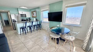A modern kitchen with a dining area, a flat-screen TV, and a view of the beach. - Time to get… 🎶 Knee deep in the water somewhere! 🎶 on island time! (Gulf Shores)