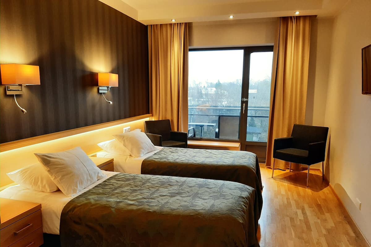 A hotel room with two beds, a desk, a chair, and a large window with curtains.