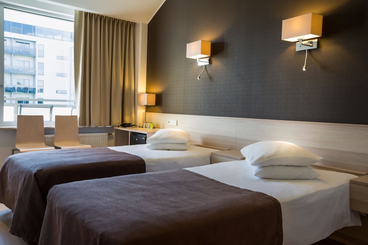 A hotel room with two beds, a desk, a chair, and a window with curtains.