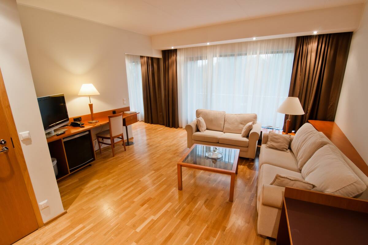 A modern living room with a wooden floor, a sofa, a coffee table, a TV, and a desk with a lamp.