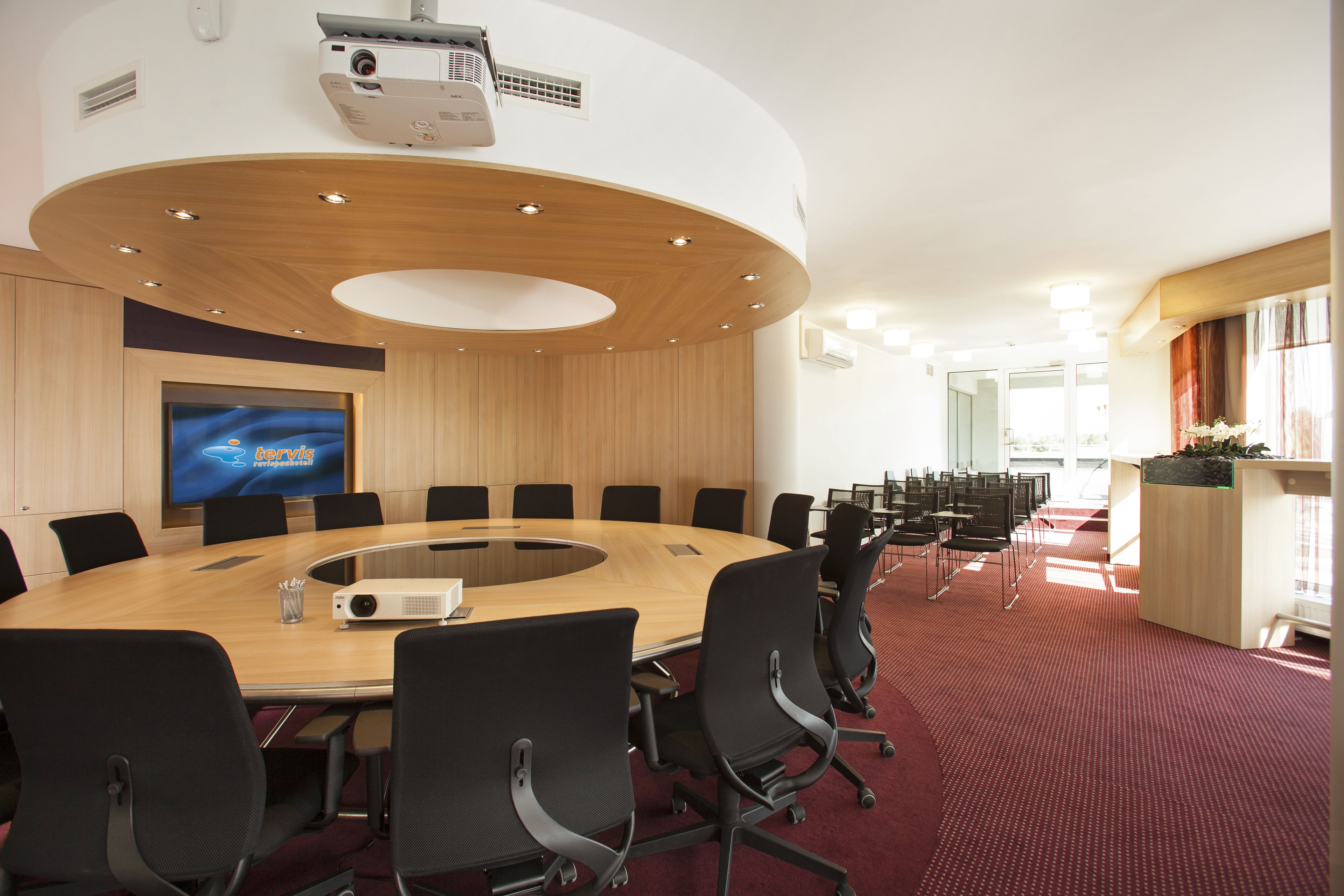 A conference room with a large oval table, black chairs, a projector, and a screen displaying 'terris'.