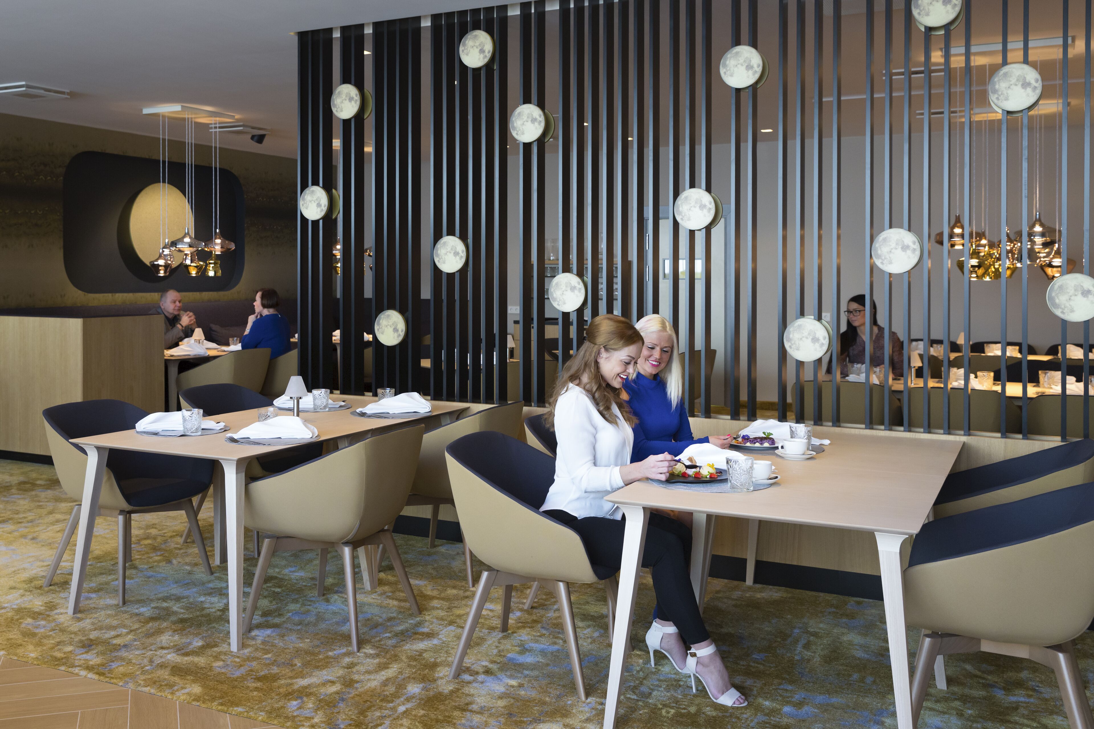 Un comedor moderno con mesas, sillas y una pared decorativa con luces colgantes.