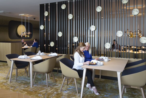A modern dining area with tables, chairs, and a decorative wall with hanging lights.