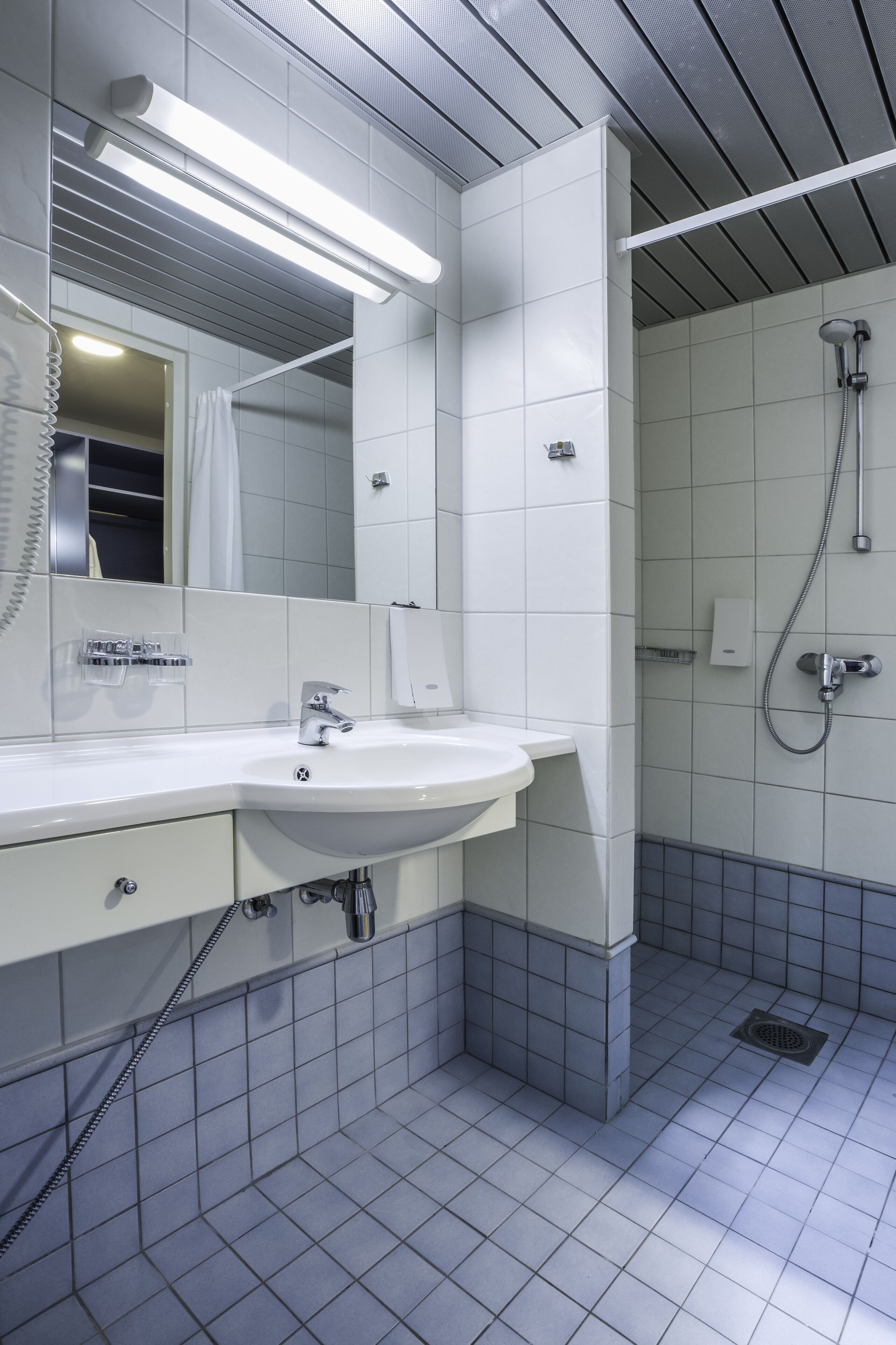 Un baño moderno con un lavamanos, espejo y ducha blancos.