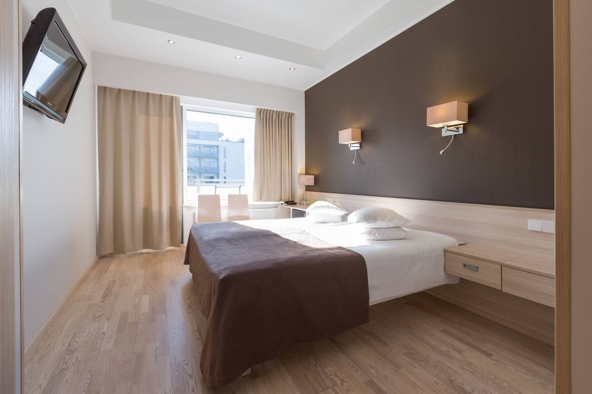 A modern hotel room with a large bed, bedside tables, a flat-screen TV, and a view of the city.