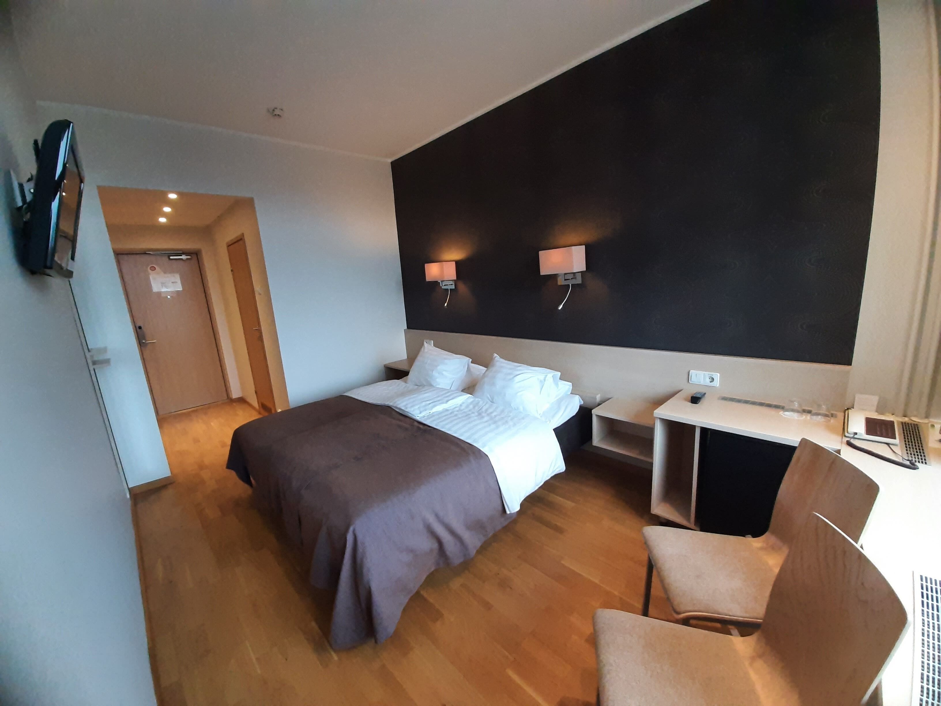 Una habitación de hotel con una cama, mesitas de noche, un escritorio y una silla.