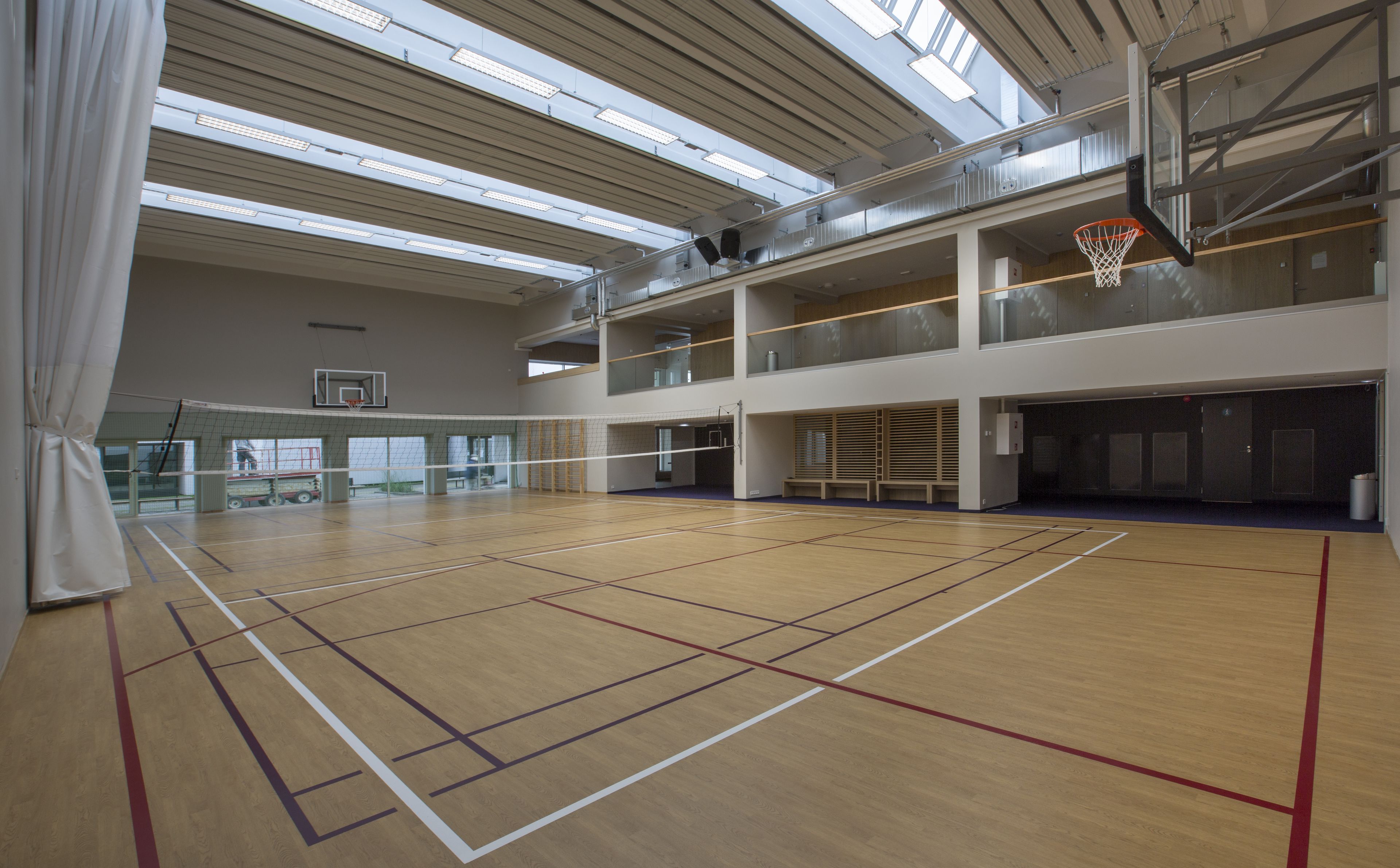 An indoor basketball court with a wooden floor, a basketball hoop, and a net.