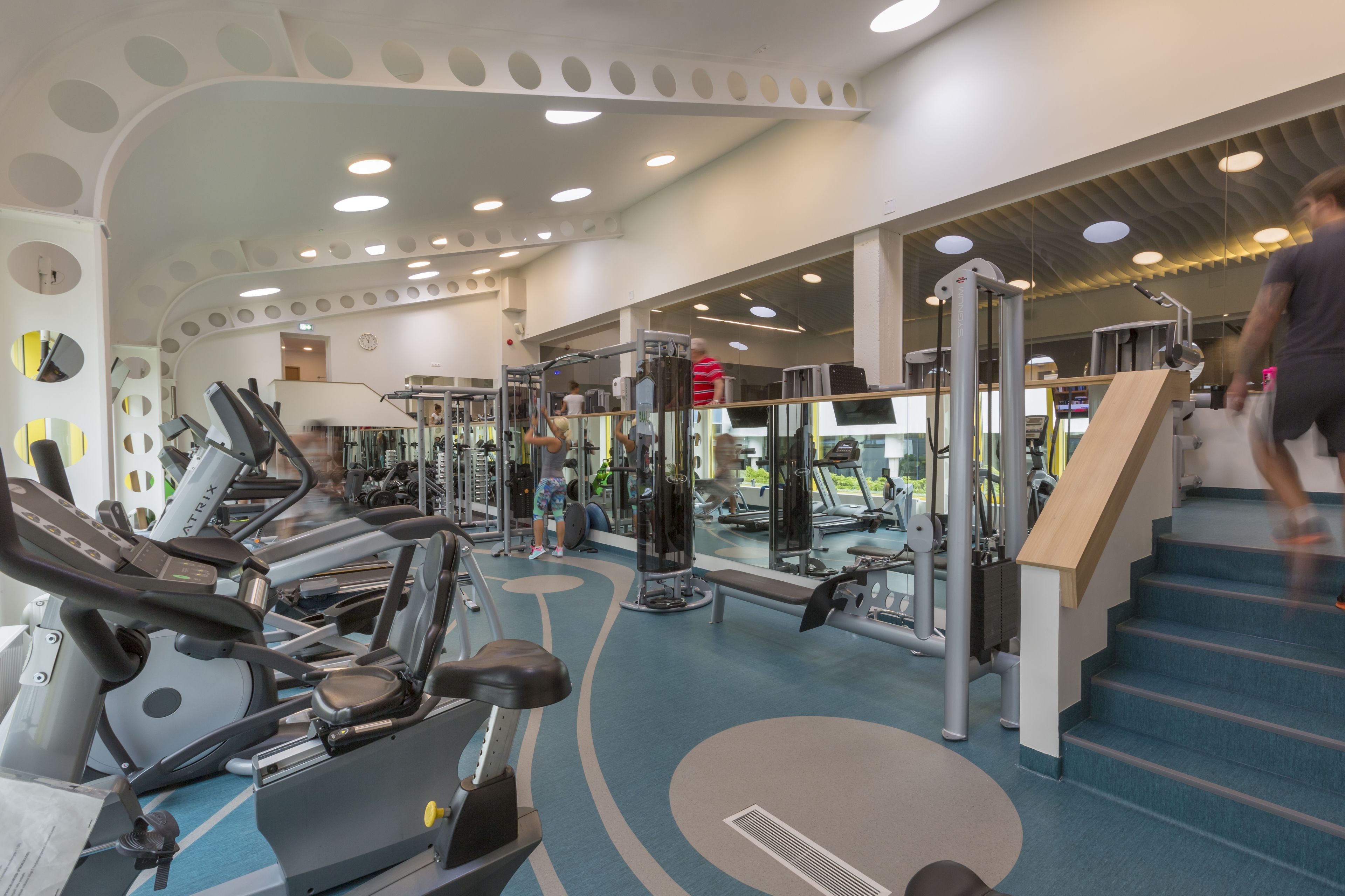 Ein Fitnessstudio mit Laufbändern, Kraftgeräten und einer Treppe.