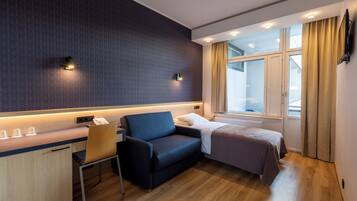 A hotel room with a desk, a chair, a bed, a window with curtains, and a wall-mounted TV.