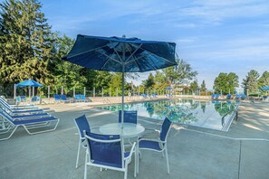 Zona de piscina con sillas de descanso, una mesa y sombrillas.