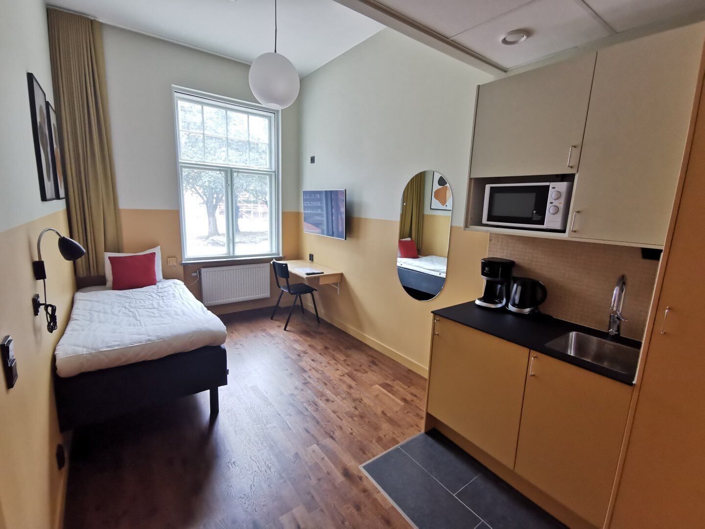 Una habitación de hotel pequeña con una cama, un escritorio, una kitchenette y un ventanal grande.