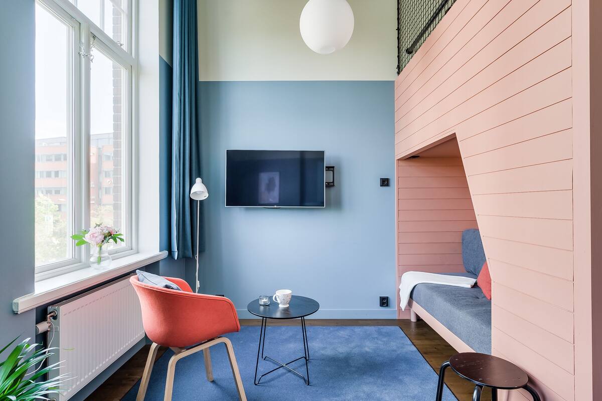 Une chambre moderne dotée d’une grande fenêtre, d’un téléviseur à écran plat, d’une petite table ronde, d’un canapé et d’un fauteuil.