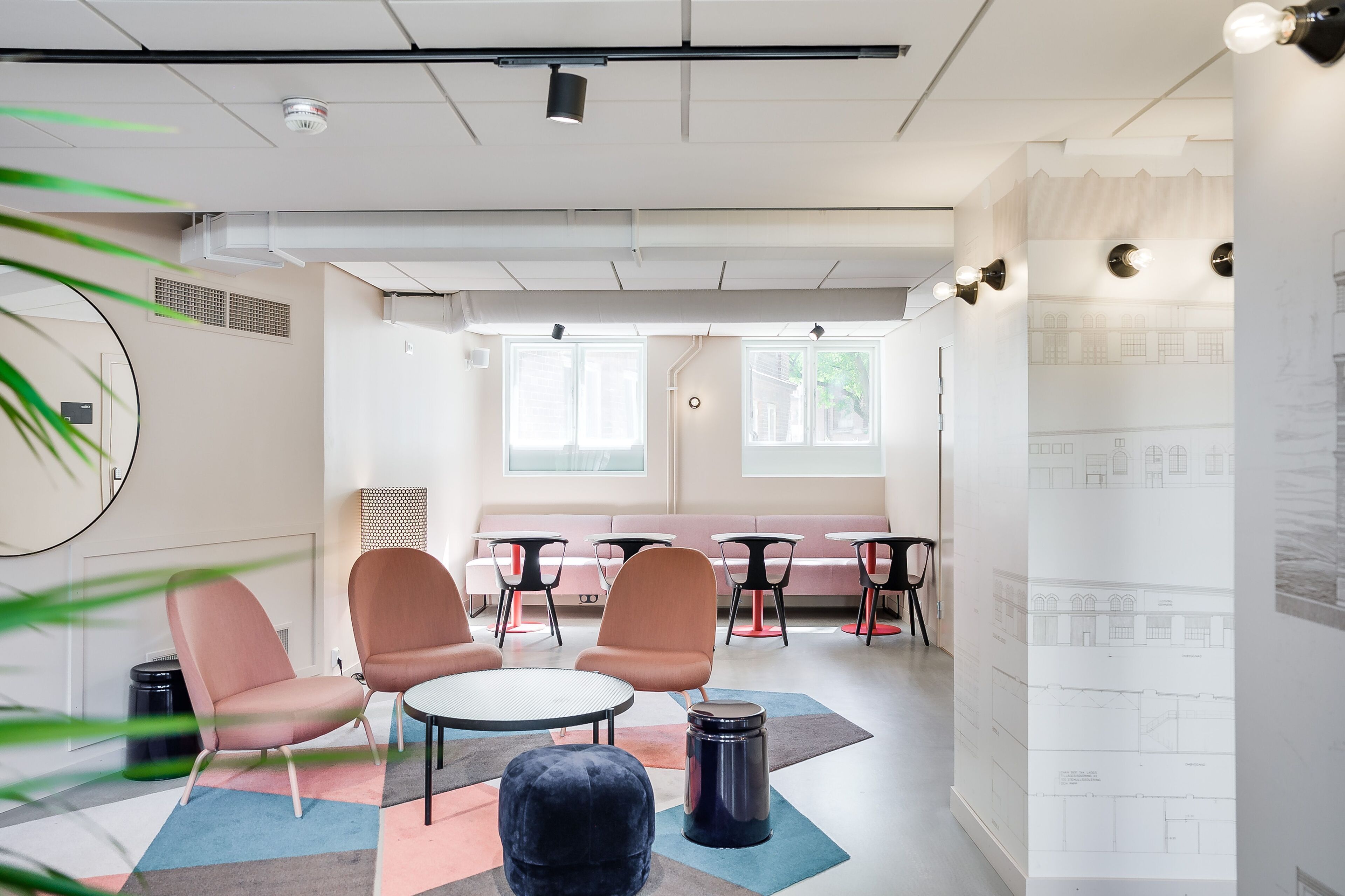 A modern meeting room with a long table, several chairs, a sofa, and a large window providing natural light.