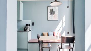 A modern kitchen with a dining area, featuring a light blue wall, a framed artwork, and a pendant light.