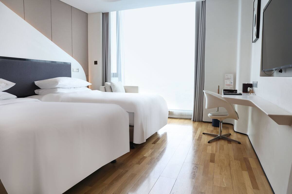 Una habitación de hotel moderna con dos camas, un escritorio y un televisor.