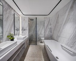 Un baño moderno con paredes de mármol, una bañera grande y una zona de ducha con mampara de cristal.