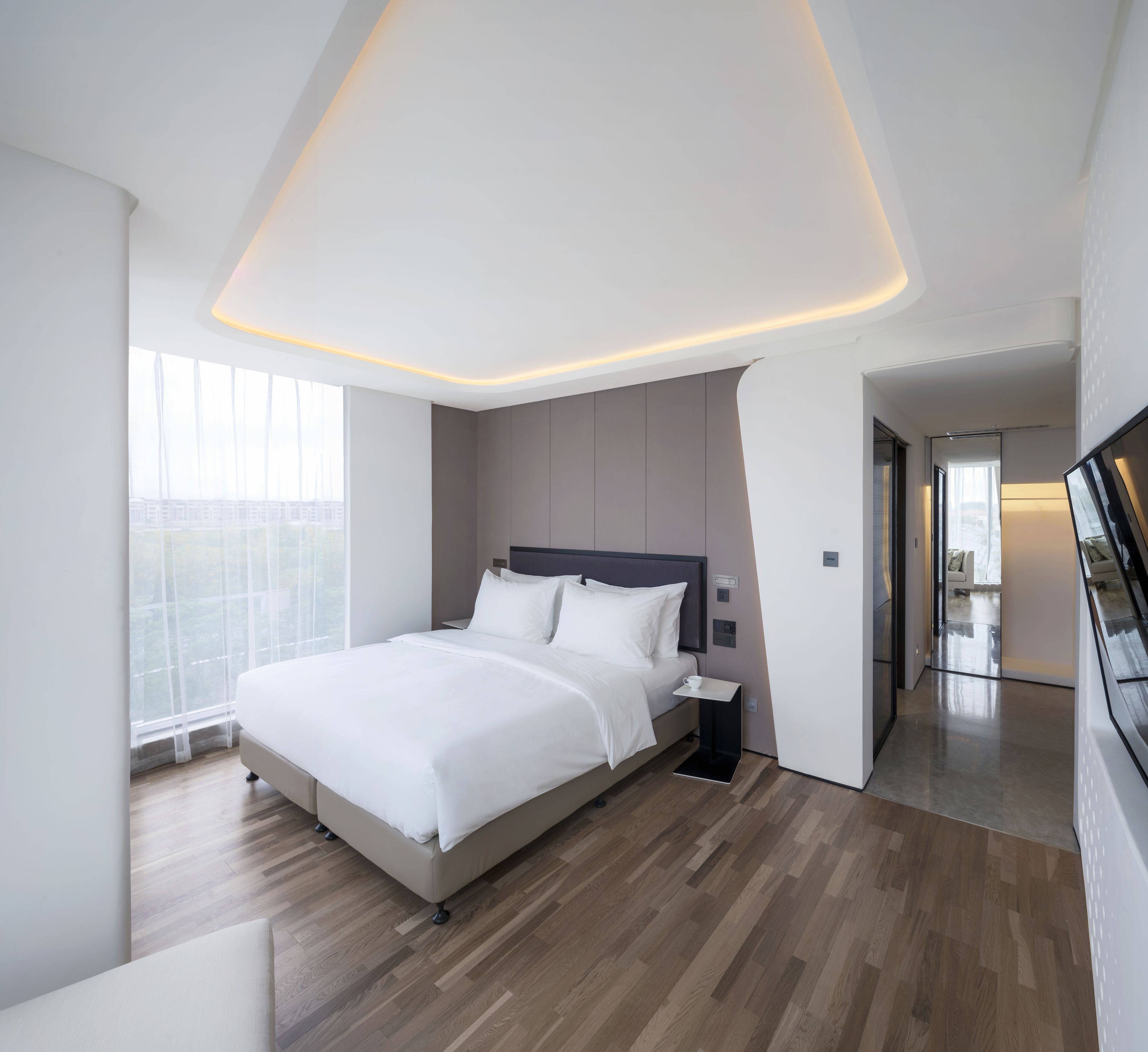 A modern bedroom with a large bed, a bedside table, and a view of the city through large windows.