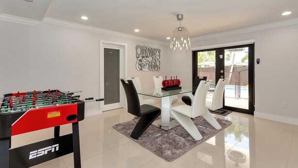 Un espace repas moderne avec une table en verre, des chaises blanches et une table de baby-foot.