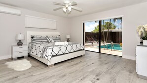 Une chambre à coucher avec un lit, un ventilateur de plafond, une table de chevet, une lampe et une vue sur une piscine.