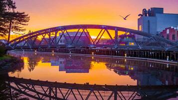 Un pont d’acier enjambant une étendue d’eau calme, avec un coucher de soleil en arrière-plan.